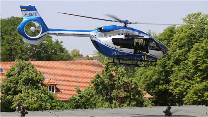 Helikopter schwebt über dem Gebäude 2 auf dem Campus. Ein Polizeibeamter seilt sich gerade ab. 