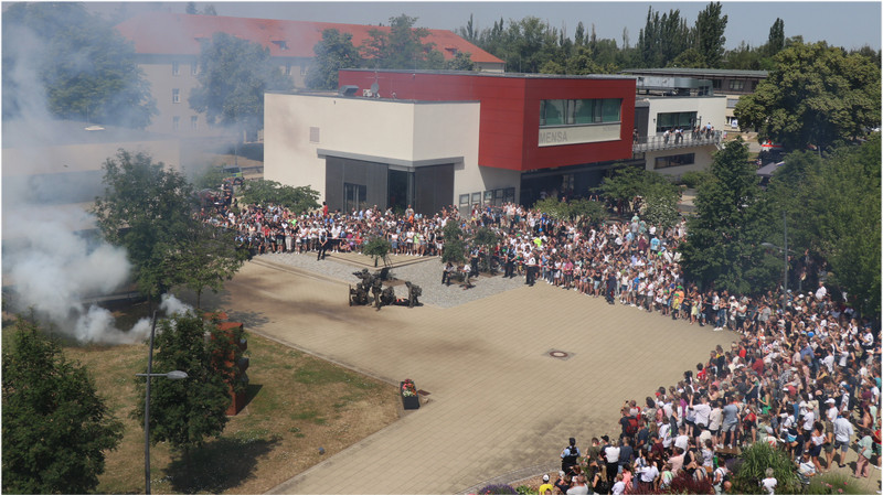 Aufnahme einer Präsentation einer Einsatzszene auf dem Campus. Zu sehen Rauchkörper, Einsatzkräfte mit Fahrzeugen und darum stehend Besucher des Tag der offenen Tür. 